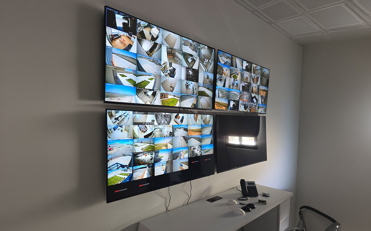 Wall-mounted CCTV monitoring station with multiple screens displaying live camera feeds above a control desk at Al-Motakamila Flexible Packaging