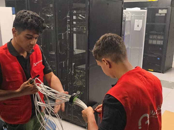 Two Iraq Gate technicians preparing a bundle of structured cabling in front of data centre racks